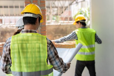 Asyalı mühendis ya da Genç Mimar güvenlik için bir kask taktı ve İnşaat Fabrikası İnşaat Alanı 'nın Şablonu' na baktı ve müteahhitle konuşmak için telsiz kullandı..