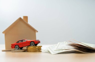 Banknotun, araba kredilerinin, ev sigortasının, ekonomik sorunların ve enflasyonun yanı sıra ahşap bir evin önündeki bozuk paraların üzerinde kırmızı minyatür araba modeli