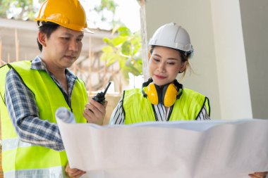 Asyalı mühendis ya da genç bayan mimar güvenlik için bir kask taktı ve bir inşaat fabrikası projesi için müteahhitle konuştu: Takım çalışması kavramı, liderlik kavramı..