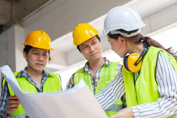 Asian engineer or Young Female Architect put on a helmet for safety and talk with a contractor on a construction building factory project, Concept of Teamwork, Leadership concept.