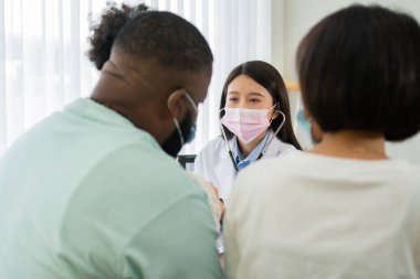 Asyalı kadın pediyatrist doktor muayene için stetoskop tutuyor küçük bir kız hasta ve çocuğun kalp ciğerleri, iyi aile doktoru çocuğu evde ziyaret ediyor, sağlık ve çocukluk konsepti için ilaç alıyor..