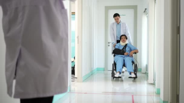 事故後に車椅子でアジアの女性患者と医師 車椅子で患者を押す外科医 事故の怪我から痛み — ストック動画
