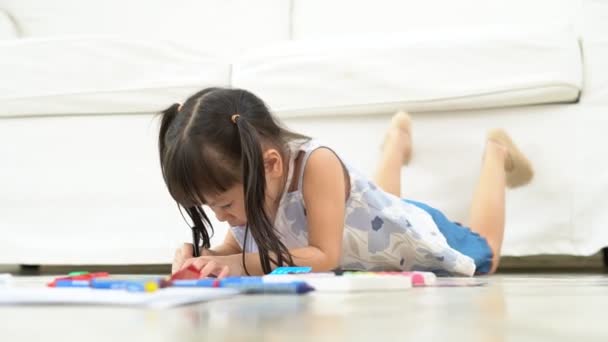 かわいいアジア系の子供の女の子は 暖かい床に横たわって 色ペンの描画や絵画を保持し 彼女は楽しんでいると笑 学習の概念と創造的な趣味 子供の発達を楽しむ — ストック動画