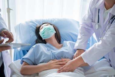 Bir grup doktor, hasta kadının hasta yatağında yatmasına ve karın ağrısına dayanmasına yardım etmeye çalışıyor. Adet, ishal ya da hazımsızlıktan kaynaklanan karın ağrısı. Hastalık ve sağlık hizmeti kavramı