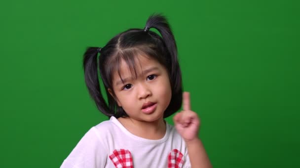 描绘了一个快乐的亚洲小女孩在绿色背景下对着相机的动作 一个小孩在看着相机 学龄前儿童的梦想充满了精力 感觉健康和好的概念 — 图库视频影像