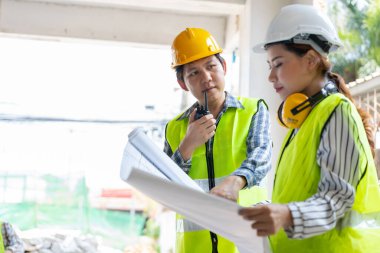 Asyalı mühendis ya da genç bayan mimar güvenlik için bir kask taktı ve bir inşaat fabrikası projesi için müteahhitle konuştu: Takım çalışması kavramı, liderlik kavramı..