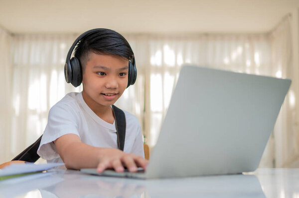 Asian boy playing guitar and watching online course on laptop while practicing for learning music or musical instrument online at home. Boy students study online with video call teachers play guitar.