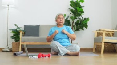 Üst düzey Asyalı kadın evdeki oturma odasında egzersiz yaparken dizüstü bilgisayarda ders izliyor. Çevrimiçi antrenman kavramı.