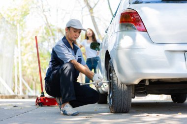 Üniformalı uzman bir tamirci, vidaları sökmeye çalışıyor vidaları sökmeye çalışıyor ve otoyolda tekerlek değiştiren bir kadına yardım ediyor, araba servisi, onarım, bakım konsepti....