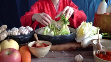 Geleneksel Kore kıyafetleri giyen Asyalı kadınlar, sarımsak, gochugaru (Kore biberi) ve taze sebze gibi malzemelerle el yapımı tuz ve Kimchi malzemeleri serpiyorlar..