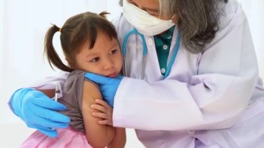 Hastanedeki Asyalı kızların omzunda aşı yapmak için şırınga tutan doktor. Pediyatrist çocuklar için aşı yapıyor. Aşılama, aşılama, hastalık önleme kavramı.