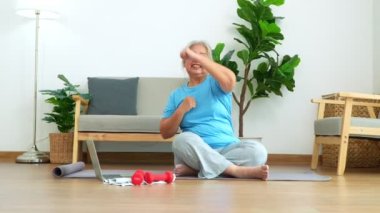 Üst düzey Asyalı kadın evdeki oturma odasında egzersiz yaparken dizüstü bilgisayarda ders izliyor. Çevrimiçi antrenman kavramı.