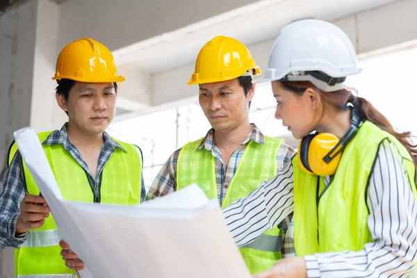 Asian engineer or Young Female Architect put on a helmet for safety and talk with a contractor on a construction building factory project, Concept of Teamwork, Leadership concept.