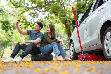 Asian couple using smartphone for assistance after a car breakdown on street. Concept of vehicle engine problem or accident and emergency help from Professional mechanic
