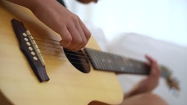 Genç Asyalı çocuk akustik gitar çalıyor. Oturma odasındaki rahat koltukta oturuyor ve favori hobisinin tadını çıkarıyor. Müzik eğitimi konsepti imajı..