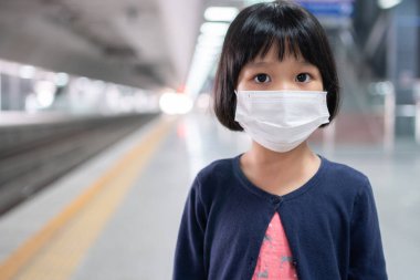 Cerrahi maskeli küçük kız, toplu taşımada (hava treni veya metro) koruma gribi ve virüs salgınıyla karşı karşıya. Yeni normal yaşam tarzı kavramı, okula gitmek için toplu taşıma araçlarını kullanmak..