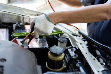 Araba aküsünü şarj etmek için akü kablosu tutan tamircinin seçici odak noktası araba aküsü, servis motoru konsepti