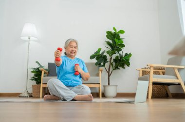 Asian senior woman lifting dumbbell for exercise and workout at home. Active mature woman doing stretching exercise in living room. Exercise Active and healthy for older, elder, and senior concept.