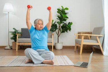 Asian senior woman lifting dumbbell for exercise and workout at home. Active mature woman doing stretching exercise in living room. Exercise Active and healthy for older, elder, and senior concept.