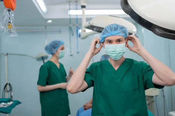 Portrait of Asian surgeon with medical mask standing in operation theater at a hospital. Team of Professional surgeons. Healthcare, emergency medical service concept