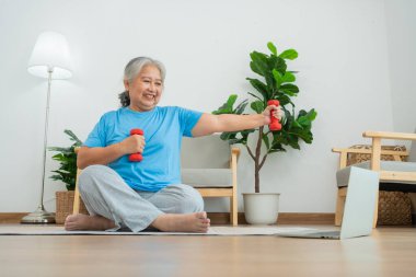 Asian senior woman lifting dumbbell for exercise and workout at home. Active mature woman doing stretching exercise in living room. Exercise Active and healthy for older, elder, and senior concept.