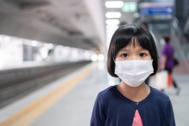 Cerrahi maskeli küçük kız, toplu taşımada (hava treni veya metro) koruma gribi ve virüs salgınıyla karşı karşıya. Yeni normal yaşam tarzı kavramı, okula gitmek için toplu taşıma araçlarını kullanmak..