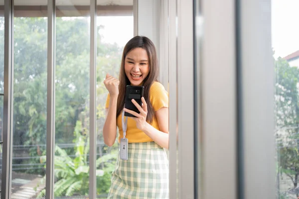 Happy young Asian women startup entrepreneur happy and excited smiling after getting message for success sign business contact, happy girl on workplace. Distance learning online education and work.