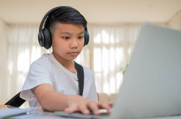 Asian boy playing guitar and watching online course on laptop while practicing for learning music or musical instrument online at home. Boy students study online with video call teachers play guitar.