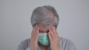 Tıbbi maske takan hasta Asyalı bir adam ve baş ağrısını tutmak için elini uzat. Korunma pandemik koronavirüs ve solunum hastalığı kavramı