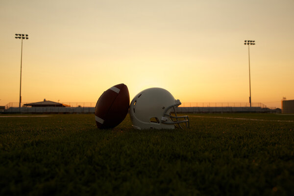 American Football and Helmet on the Field at Sunset