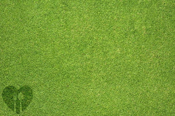 Spoon with heart icon on green grass texture and background — Stock Photo, Image