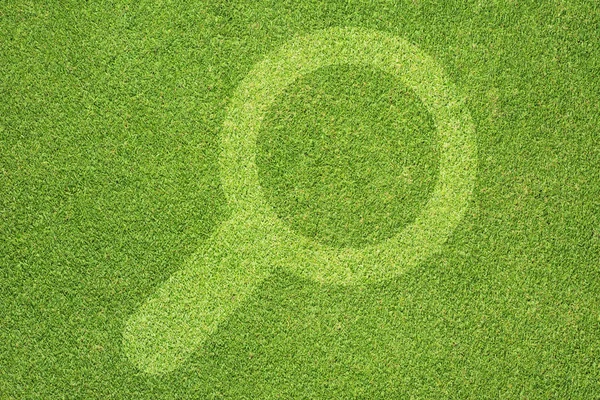 Увеличение иконки стекла на зеленом фоне травы — стоковое фото