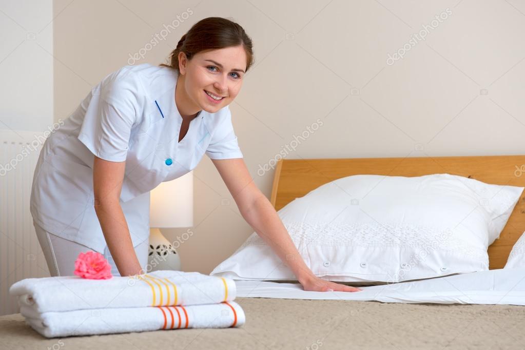 Maid making bed in hotel room