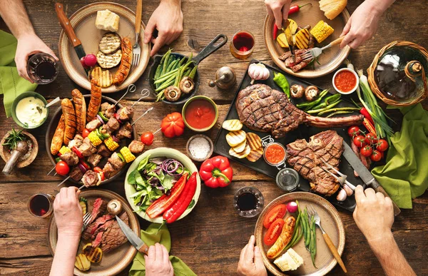 バーベキューパーティーをする友達 素朴なピクニックテーブルでグリルした肉や野菜を食べ ワインを飲む人々のグループ — ストック写真