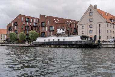 Danimarka, Kopenhag 'da parlak bulutlu bir ışıkta çekilen eski mavna ve tuğla duvarlı binalarla dolu bir şehir manzarası.