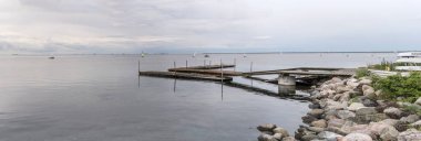 Dragor, 20 Haziran 2022, Öresund kıyılarında rıhtımı ve sakin sularda yüzen tekneleri olan şehir manzarası, 2022 Haziran 'ında Danimarka' nın Dragor kentinde açık bulutlu bir ışık altında vuruldu.