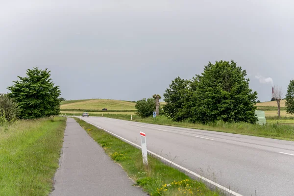 landscape with coastal road and side cycle lane at green shore of Oresund sea, shot in bright cloudy light near Niva, Denmark