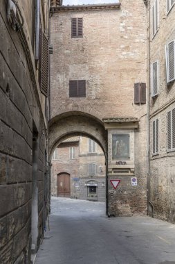 cityscape with arched passage on street among old buildings, shot in bright summer light at Siena, Tuscany,  Italy