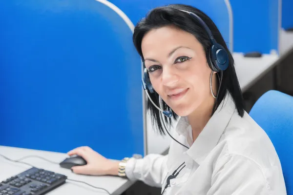 Sonriente operador de centro de llamadas chica sentada en el escritorio con el ordenador —  Fotos de Stock