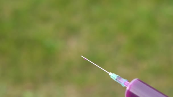 From the needle of a medical syringe, a saturated purple liquid is poured in drops. Close-up in slow motion on a green background — Stock Video