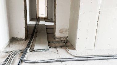 Tamamlanmamış bir odanın zemininde elektronik iletişim kabloları var. Kablolar ve borular