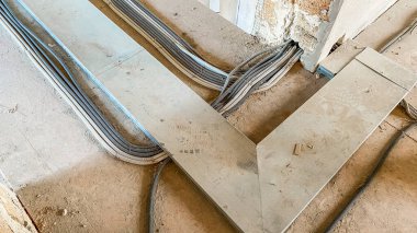 Tamamlanmamış bir odanın zemininde elektronik iletişim kabloları var. Kablolar ve borular