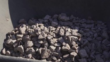 Kürek, inşaat el arabasına ağır çekimde moloz atar. Toz uçar