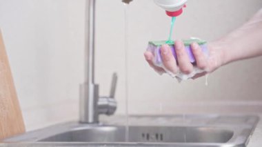 El, süngerin üzerine sıvı deterjan döker ve bulaşıkları yıkamaya başlar.