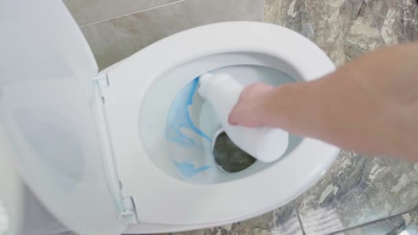 A hand sprays a toilet bowl with blue detergent. Disinfection and odor removal in the toilet, top view — Stock Video