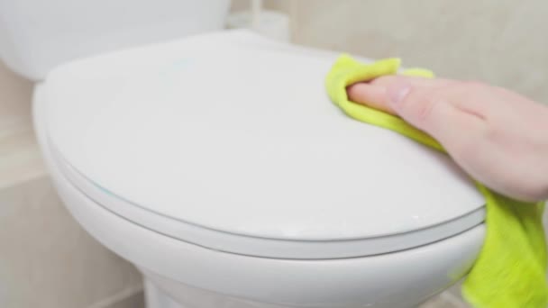 Közelkép egy kézről, amint sárga ronggyal letörli a WC fedelét. — Stock videók