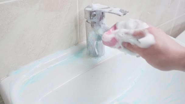 Una mano frota completamente el detergente espumoso sobre el lavabo y el grifo del baño con una esponja. Lavando el manillar y el grifo — Vídeos de Stock