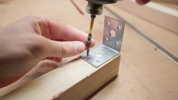 Przykręcanie metalowego rogu do drewnianego bloku czarną śrubą samogwintującą i elektrycznym śrubokrętem zbliżeniowym — Wideo stockowe