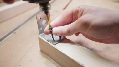 Screwing a metal corner to a wooden bar with self-tapping screws using an electric screwdriver