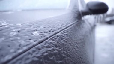 Close-up of the front fender of a black car covered with ice. Surface icing